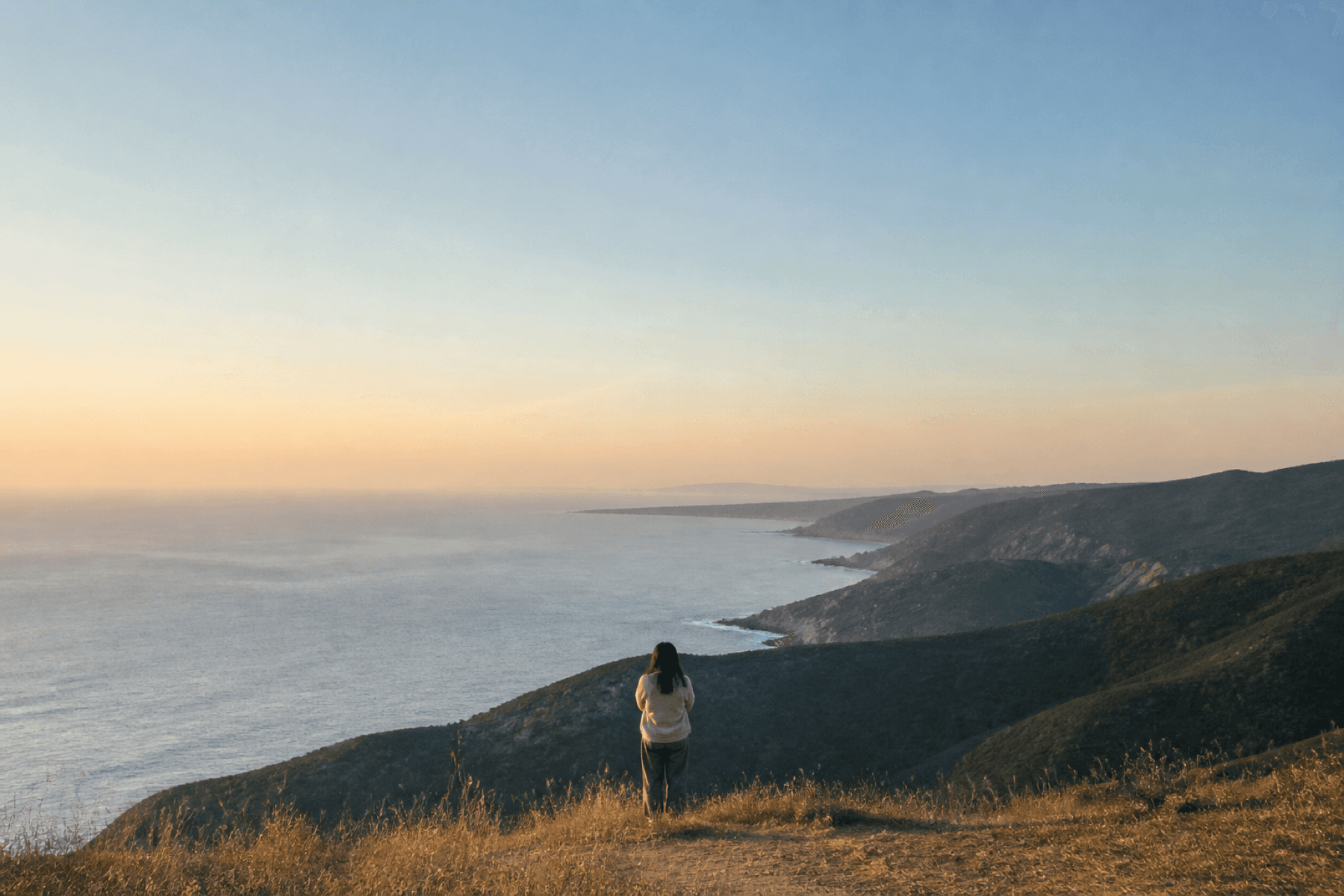 A person looking over a quiet coast at golden hour